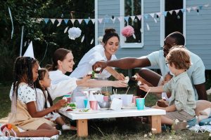 family in pastel clothes having a picnic with party banners in a backyard