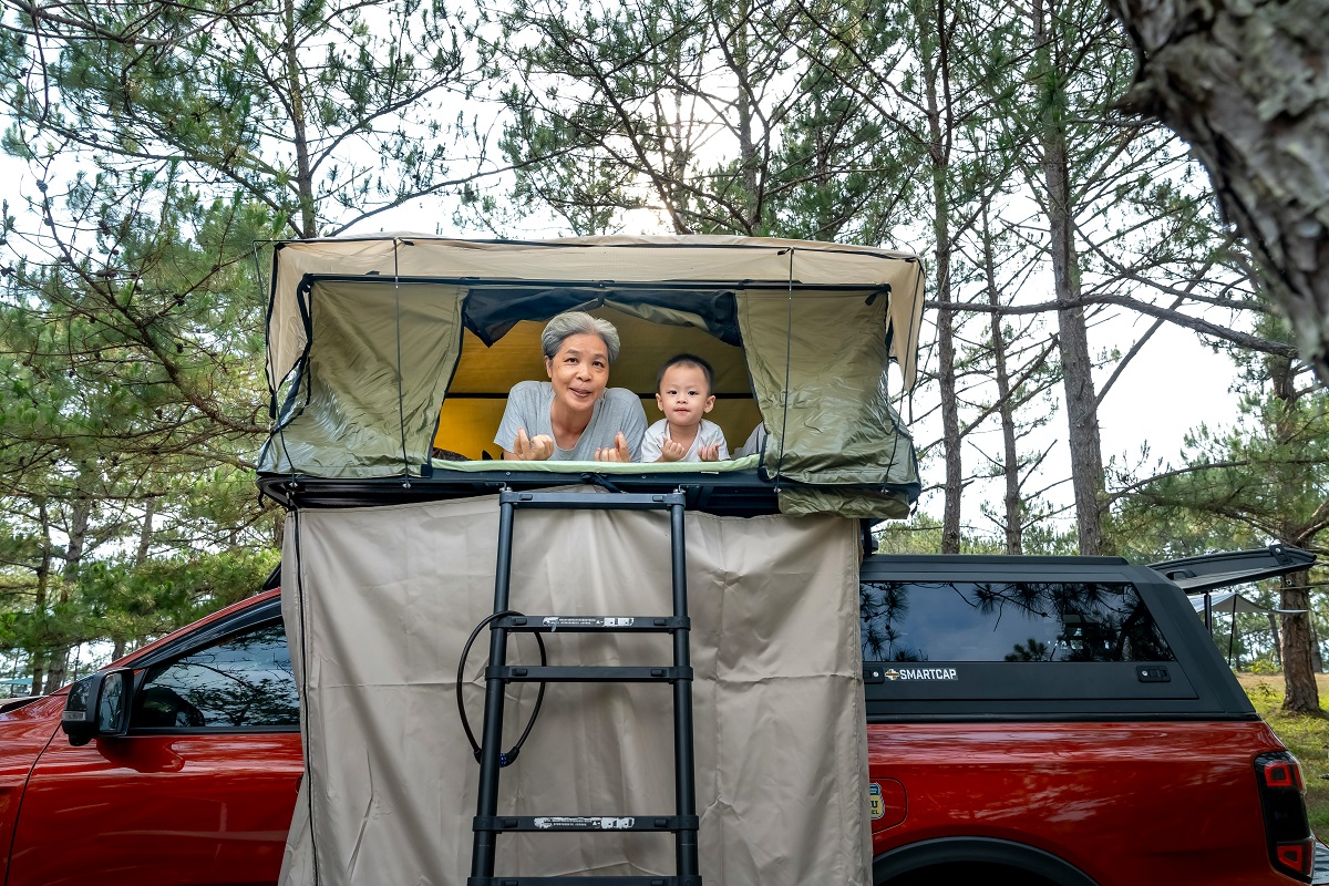 grandmother and grandson in a rooftop tent over a red car
